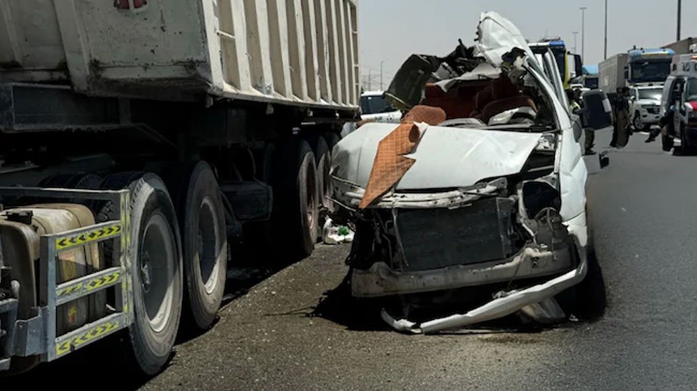 DubaiAcci Sampoorna News White sedan severely damaged after colliding with a large truck trailer on a highway debris and damaged bumper in the road responders in the background