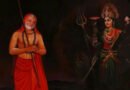Painting of a sage with a staff and beads standing beside the goddess Durga with weapons in a dark scene